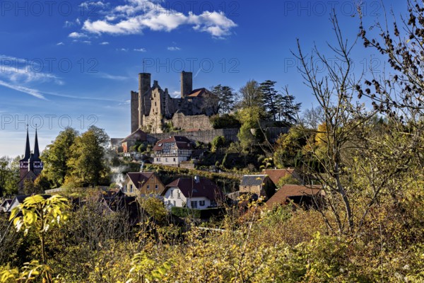 Castle above a village with a church, surrounded by autumn trees under a blue sky, Hanstein Castle near Bornhagen in the Eichsfeld district of Thuringia