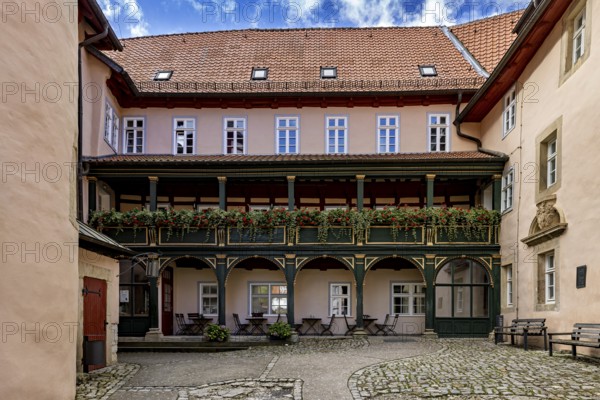 A quiet courtyard with historic half-timbered elements, balconies and decorative flowers under a blue sky, The courtyard of Bodenstein Castle in Eichsfeld, Thuringia