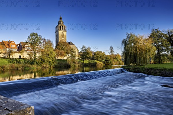 A church on the river with a small waterfall in the foreground and autumn trees in the background, the town of Bad Sooden Allendorf an der Werra in the Werra Meissner district of Hesse