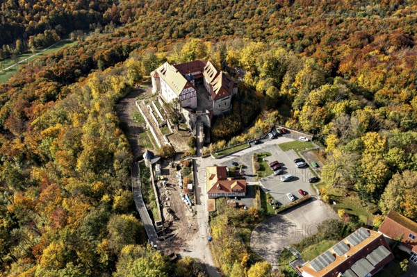 Aerial view of a castle in the autumn landscape with adjacent parking lot, surrounded by colorful trees, Bodenstein Castle in the Eichsfeld district of Thuringia