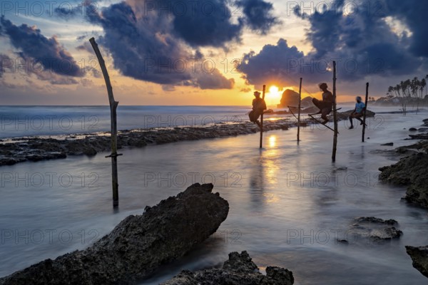 Fishermen fish at sea at sunset, the clouds are dramatically illuminated, Koggala beach with stilt fishermen in Sri Lanka