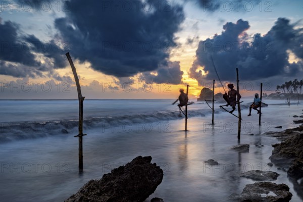 Silhouette of fishermen at sunset over the blue and orange sea, Koggala beach with stilt fishermen in Sri Lanka