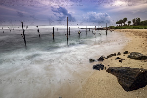 Dramatic sunset on the beach with stilts and waves, Koggala beach with stilt fishermen in Sri Lanka