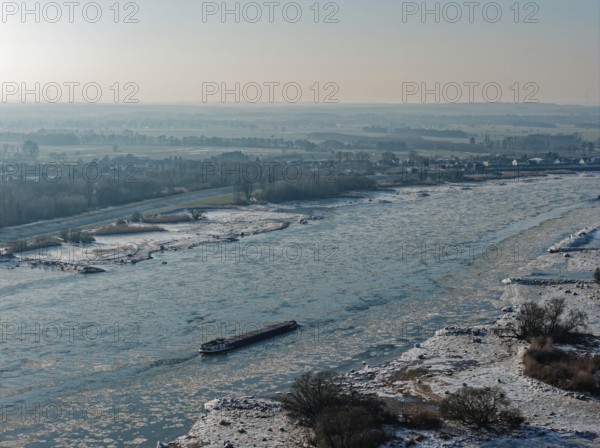 On a cold winter day, a barge sails downstream on the Elbe near Hamburg when there is slight ice. The foothills of the Elbe are icy in the flooded area. Kirchwerder, Hamburg, Germany