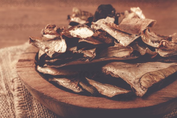 A collection of dried mushrooms fills a wooden bowl placed on a cloth surface. The mushrooms are cut into thin slices, ideal for adding to various dishes