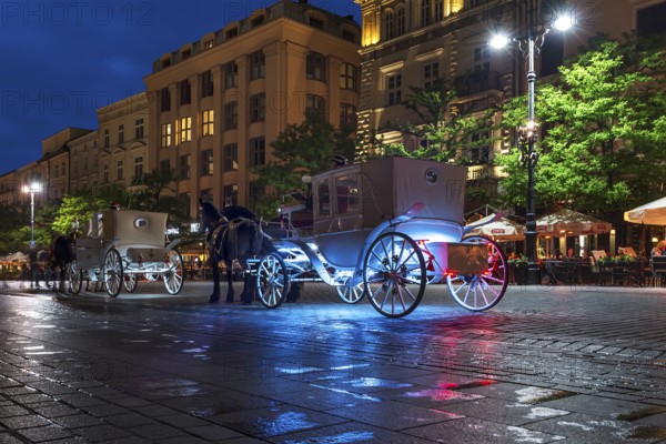 Waiting horse-drawn carriages at the market square at night, Krakow, Poland