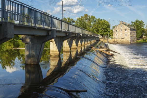 Moulin Neuf water flow control dam and walkway over Des Mille-Iles river plus New Mill on Ile des Moulins in summer, Old Terrebonne, Quebec, Canada