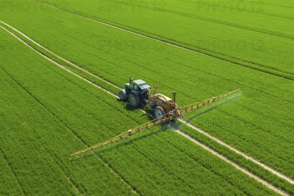 Aerial view over agricultural trailed field sprayer pulled by tractor spraying crop on farmland, field with pesticides, insecticides in spring