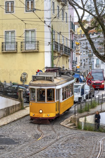 Traditional vintage yellow tram on tram line 28 climbing steep cobbled street in the capital city Lisbon / Lisboa, Portugal