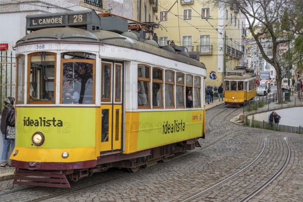 Traditional vintage yellow trams on tram line 28 climbing steep cobbled street in the capital city Lisbon / Lisboa, Portugal