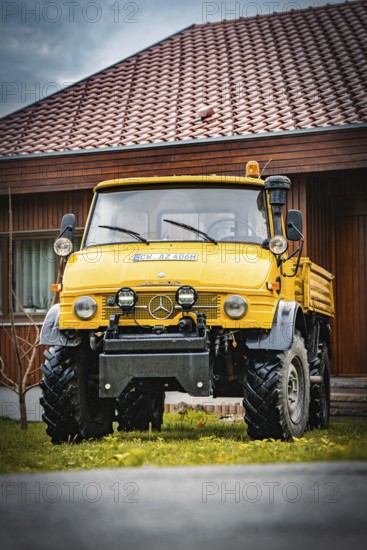 Yellow Unimog with four-wheel drive on a lawn in front of a wooden house, tree work, Gechingen, Calw district, Germany