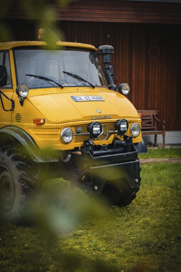 Yellow Unimog in the rain next to a wooden building in a meadow, tree work, Gechingen, Calw district, Germany