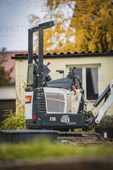 Small excavator in a courtyard next to a building in autumn, tree work, Gechingen, Calw district, Germany