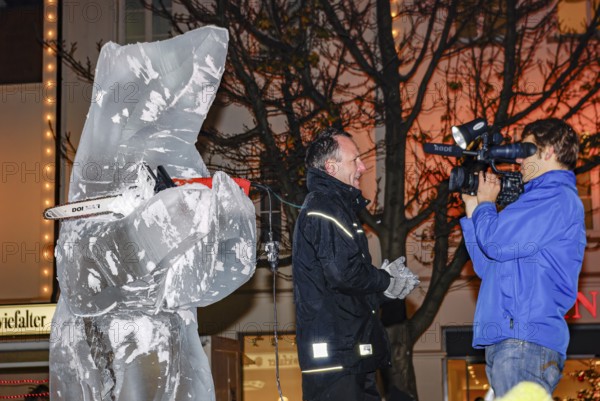 Ice carving artist in front of his ice sculpture interviewed by a GEA reporter during ice carving street action as part of the long shopping night in downtown Reutlingen, Baden-Württemberg, Germany, for editorial use only