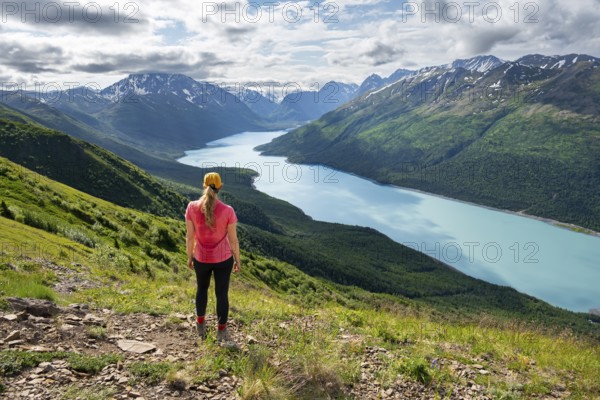 Female mountaineer enjoying views of blue lake and mountains on Twin Peaks Trail, Eklutna Lake, Chugach Mountains, Chugach State Park, Alaska, USA