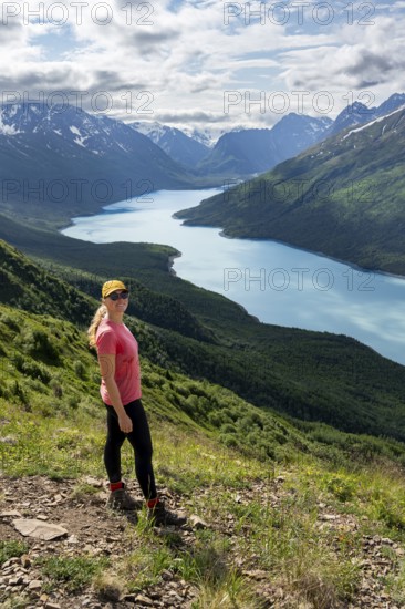 Female mountaineer enjoying views of blue lake and mountains on Twin Peaks Trail, Eklutna Lake, Chugach Mountains, Chugach State Park, Alaska, USA
