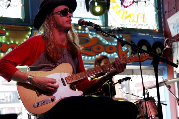 Musician wearing hat and sunglasses, playing guitar on stage in front of colorful window decoration, Nashville, Tennessee, USA