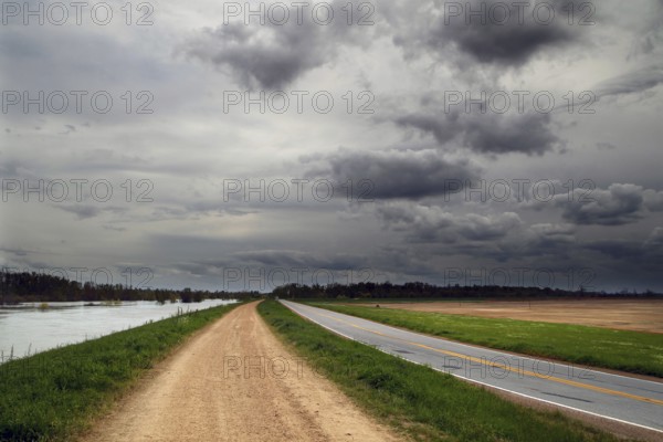 Gravel road along a river under dramatic sky, Mississippi, USA