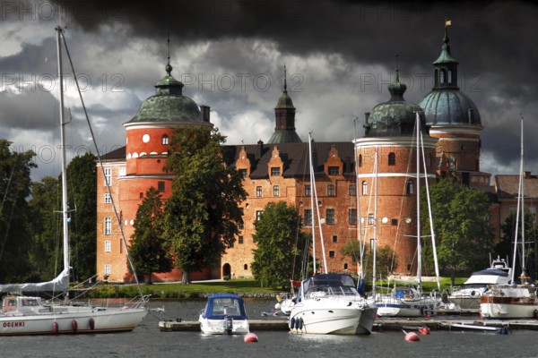 Gripsholm Castle in Mariefred against a cloudy sky with adjacent boats, Mariefred, Södermanland, Sweden