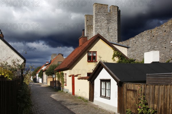 Alley with traditional half-timbered houses and towers of the city wall in Visby under threatening clouds, Visby, Gotland, Sweden