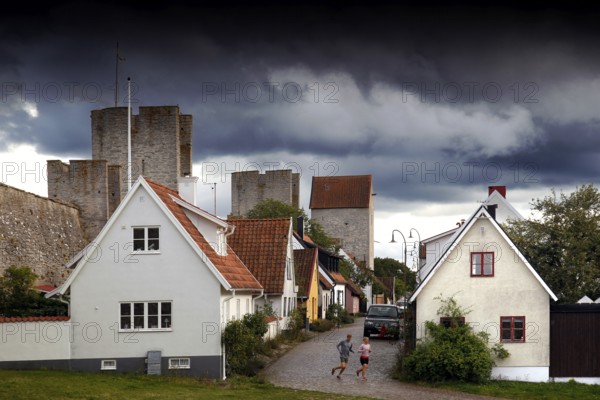 Alley in Visby's old town with historic buildings and city wall towers under a dramatic sky, Visby, Gotland, Sweden