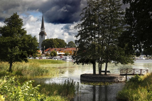 Atmospheric landscape with lakeside church surrounded by trees and clouds, Mariefred, Södermanland, Sweden