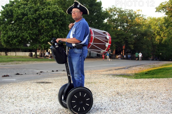 Man in period clothing rides on Segway and carries a drum, a rare sight, Williamsburg, Virginia, USA