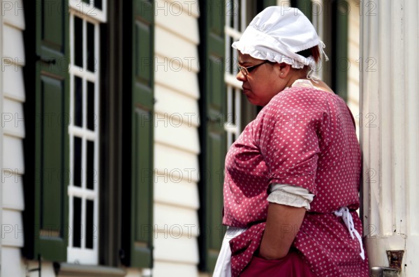 Woman in period clothing looking at a building in Colonial Williamsburg, an impression from colonial times, Williamsburg, Virginia, USA
