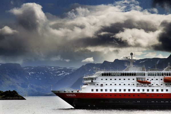 A Hurtigruten ship against a dramatic backdrop of clouds in Øksfjord, Øksfjord, Norway