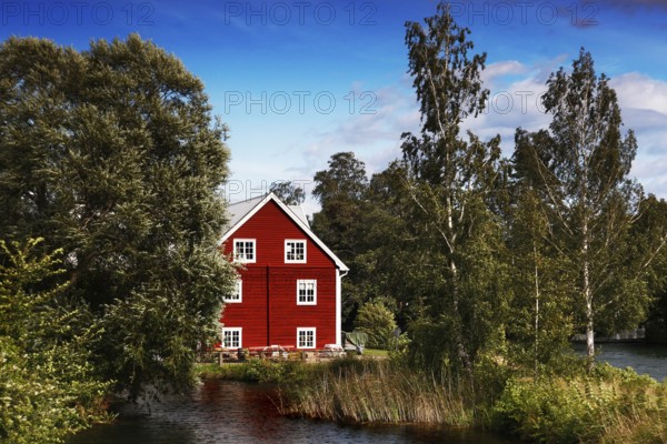 Red house on the riverbank surrounded by lush nature and clear skies, Borensberg, Sweden