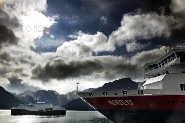 Hurtigruten ship near Øksfjord against dramatic sky and mountains, Øksfjord, Norway
