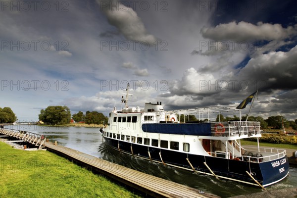 Passenger ship in the Göta Canal at a dock under a cloudy sky, mountain, Sweden