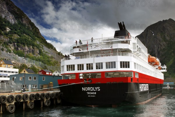 Hurtigruten ship in harbor with surrounding buildings and mountainous landscape, Øksfjord, Norway