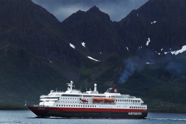 Hurtigruten ship against dramatic mountain backdrop and cloudy sky, Øksfjord, Norway