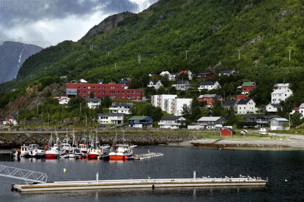 Quiet harbor with small boats and surrounding colorful houses in mountainous landscape, Øksfjord, Finnmark, Norway