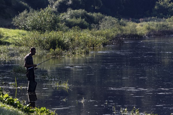 An angler stands patiently on the banks of the Nemunas River in Vilkija, Vilkija, Lithuania
