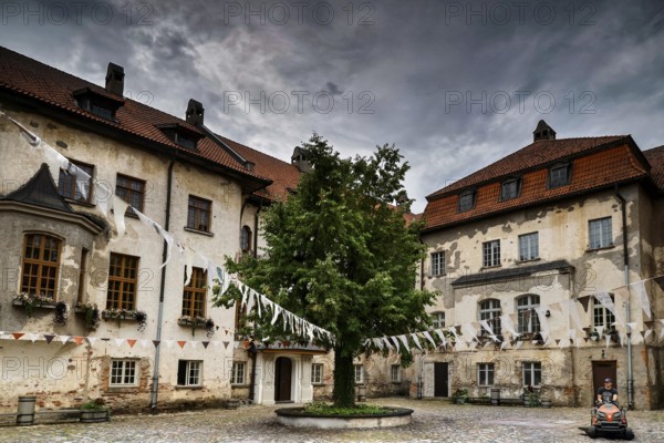 Historic castle with courtyard and central tree under dramatic sky, Dundaga, Latvia