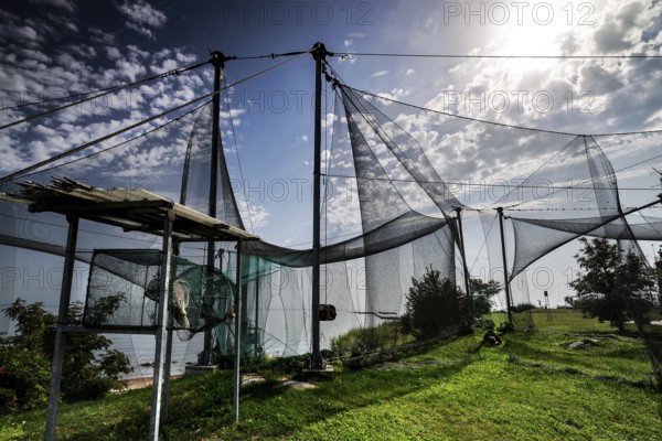 Bird observatory with nets under cloudy sky and sunlight on green terrain, Windenburg, Vente, LT