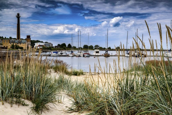View of beach and harbor with boats and lighthouse in sandy dune landscape, Engure, Latvia