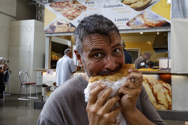 Man enjoying cheburek in the lively Central Market of Riga, Riga, Latvia