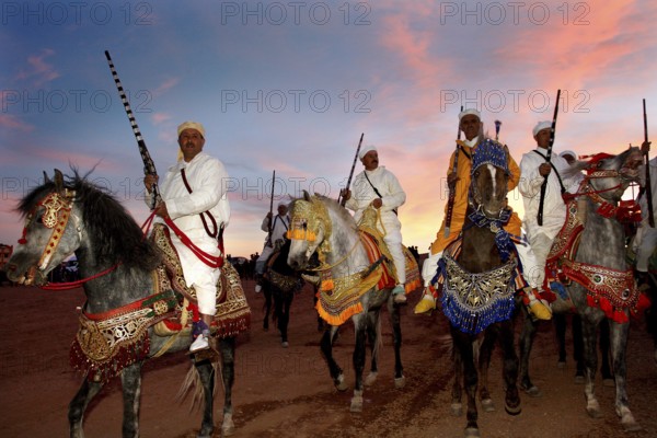 Riders wearing traditional clothes at sunset during a Fantasia performance, El Kelâa m'Gouna, Morocco