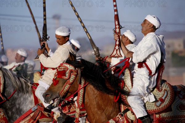Group of riders wearing traditional clothing hold up rifles at a historic Fantasia event, El Kelâa m'Gouna, Morocco