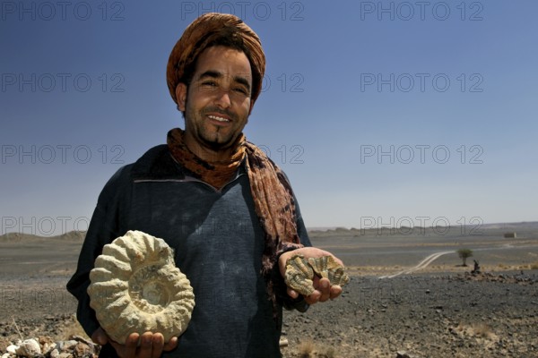 A dealer presents fossils in the desert landscape of Erfoud, Erfoud, Niger, Morocco