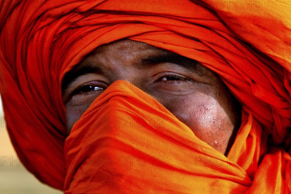Portrait of a Bedouin wearing a bright orange turban in the Erg Chebbi Desert, Erg Chebbi, Morocco