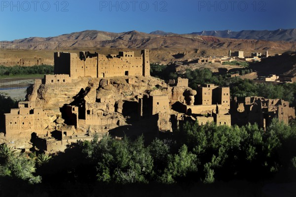 Clay buildings of the Kasbah in the Valley of Roses with surrounding mountain landscape under blue sky, El Kelâa m'Gouna, Morocco