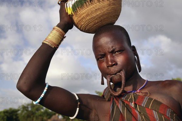 Morsi woman carries a basket on her head and has a lip plate in Mago National Park, Mago National Park, Ethiopia