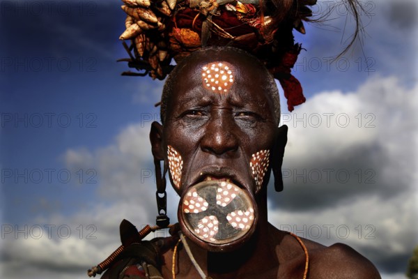 Mursi woman with lip plate and traditional headdress under dramatic sky, Mago National Park, Ethiopia