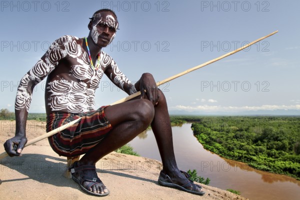 Oytade sitting with a spear, overlooking the river in the village of Murle, Murle, Ethiopia