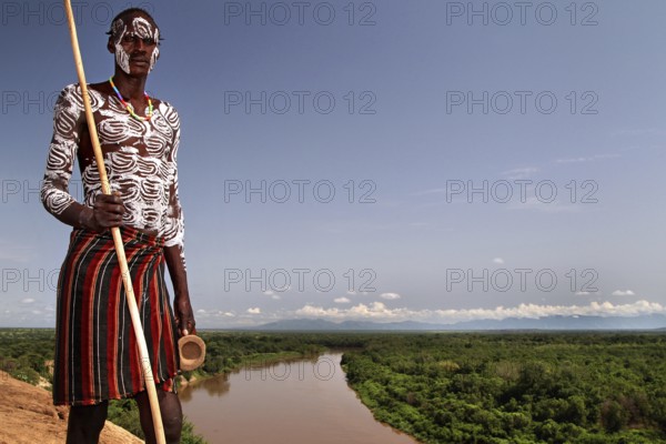 Man wearing traditional clothing looks at a river in Murle village, Murle, Ethiopia