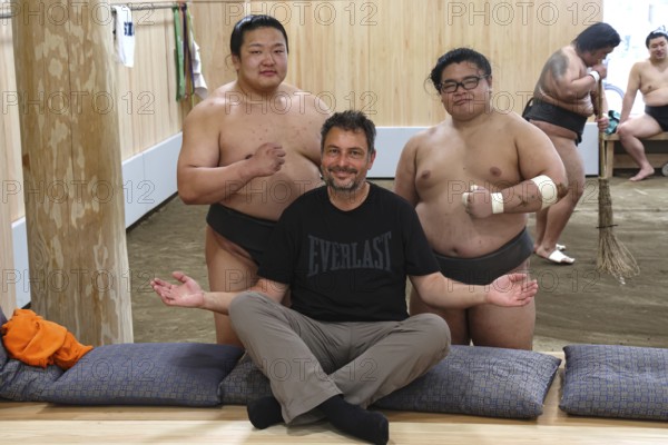 Man sitting smiling in front of two sumo wrestlers at Ryogoku training center, Tokyo, Ryogoku, Japan